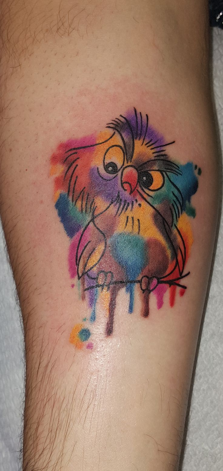 an owl tattoo on the arm with colorful paint splattered all over it's body