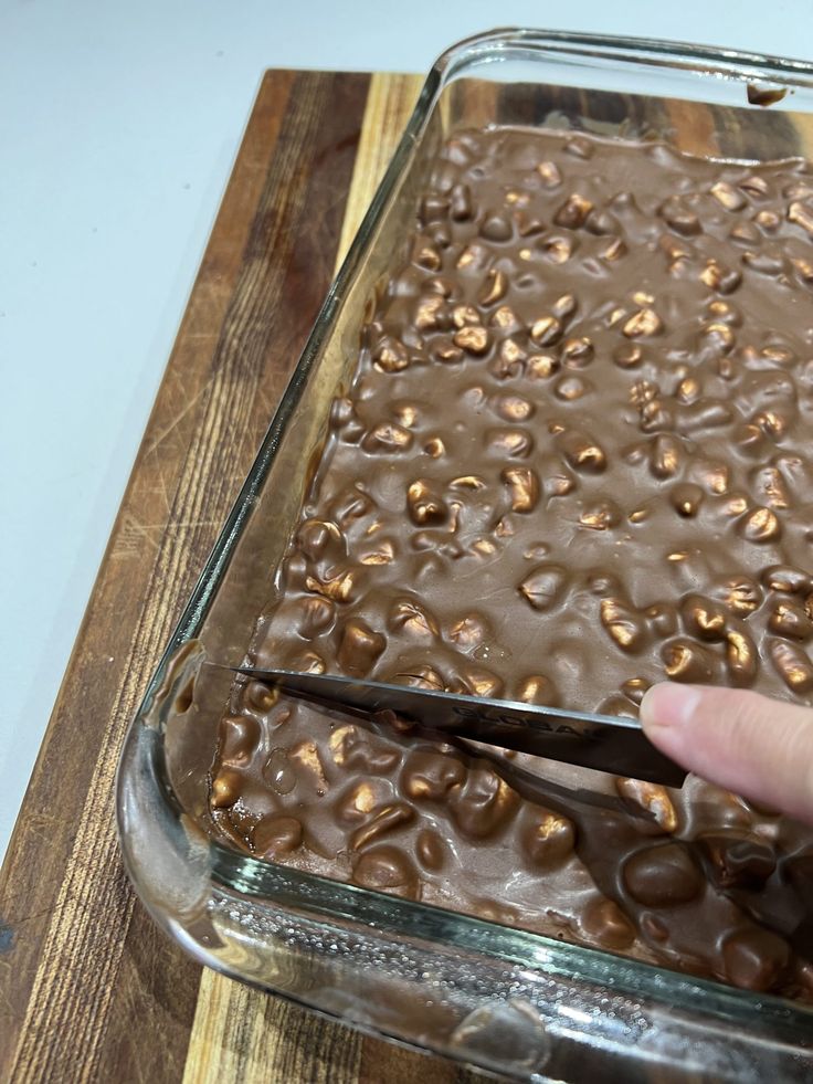 a person cutting up some food in a glass dish on top of a wooden board