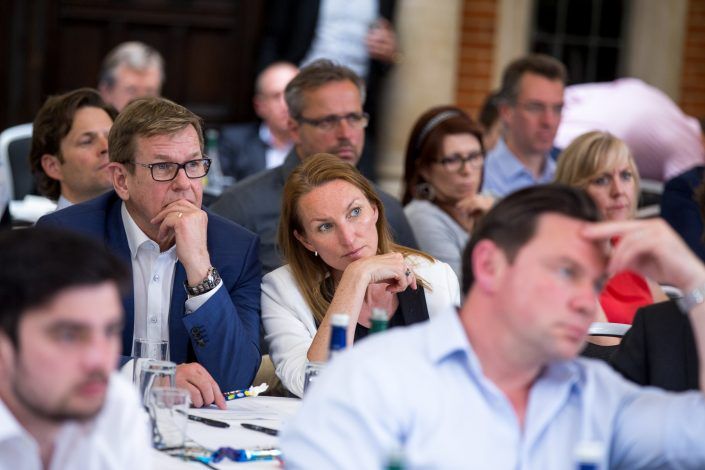 many people are sitting at tables and one is looking off to the side with his hand on his chin