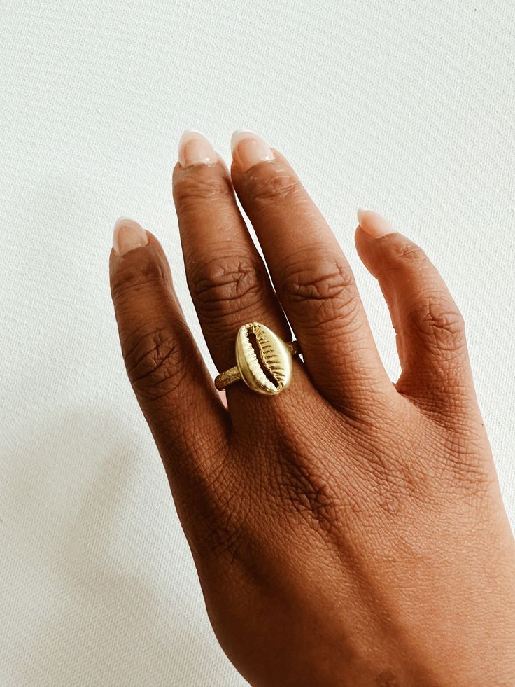 A beautiful brass cowrie shell with a lightly textured adjustable ring band. The cowrie shell represents Goddess protection, as well as symbolizes the power of destiny and prosperity. It is perfect worn alone or with a few of our stack rings.DETAILS:Available in brass or gold plated brass Adjustable Ring Band Ships with sample polishing cloth Packaged for gift giving *Sold individually, not a set. Adjustable Gold Shell Ring, Adjustable Open Ring Jewelry For Beach, Adjustable Open Ring Jewelry For The Beach, Adjustable Midi Rings For Beach, Gold Shell Rings For Beach, Handmade Gold Rings For Beach, Handmade Gold Rings For The Beach, Cowrie Shell Jewelry, African Dolls