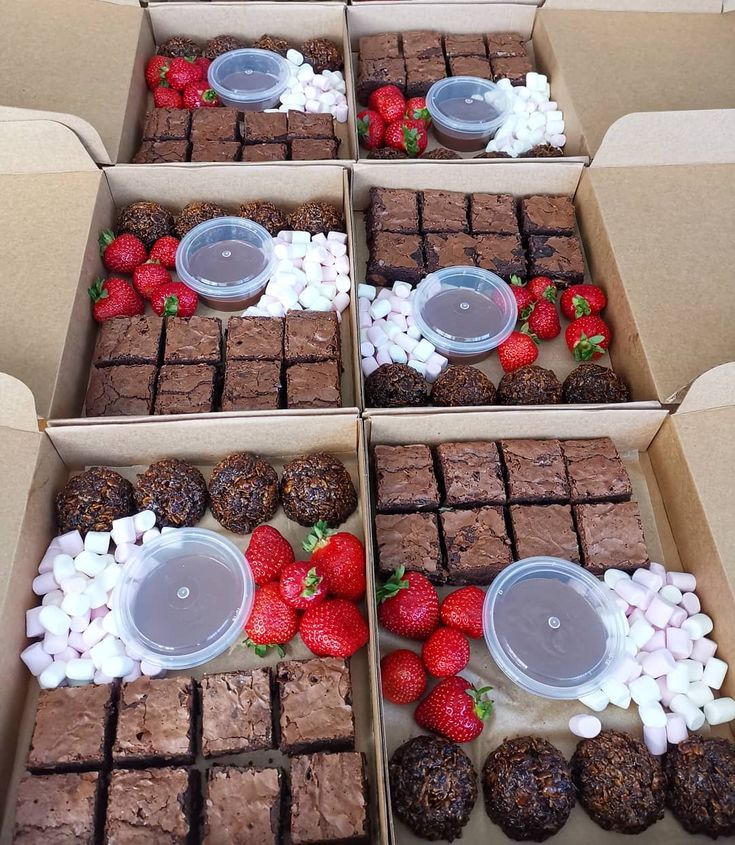 four boxes filled with brownies and strawberries on top of each box are decorated with marshmallows