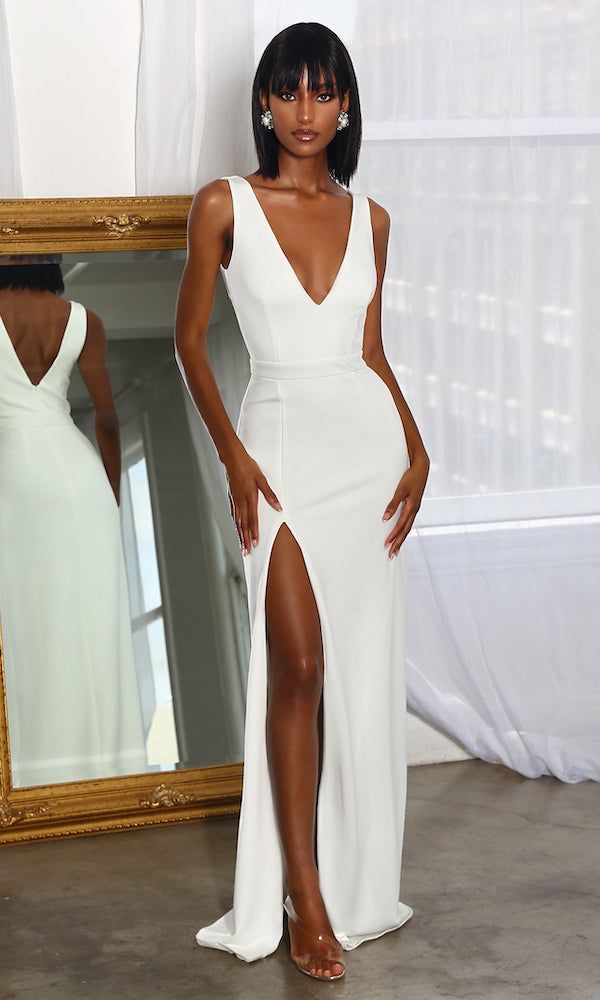 a woman standing in front of a mirror wearing a white dress with thigh high slit