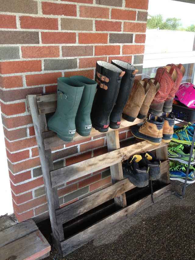 several pairs of boots are lined up on a wooden bench in front of a brick wall