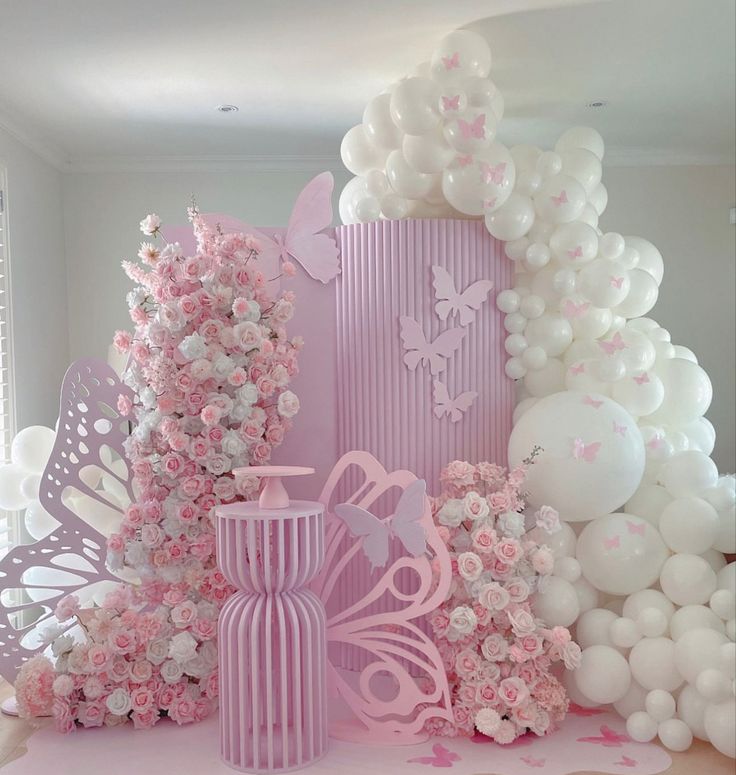 a pink and white room with balloons, flowers, and vases on the floor