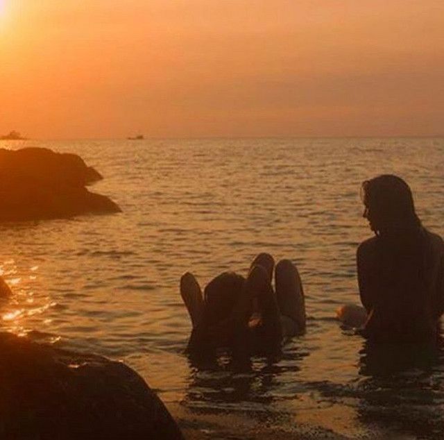 two people are sitting in the water with their backs to each other as the sun sets