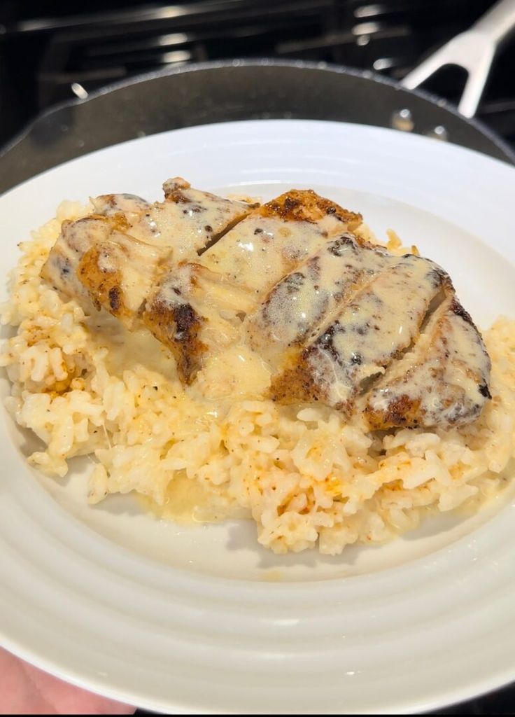 a white plate topped with rice and meat covered in gravy on top of a stove