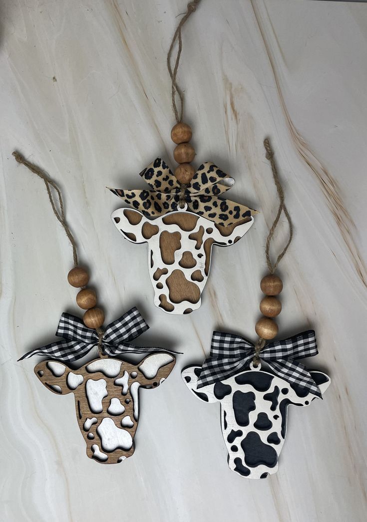 three wooden ornaments are hanging on a marble surface with black and white patterns, one has a giraffe's head in the middle