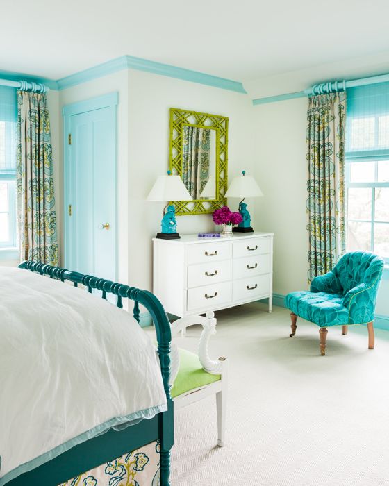 a bedroom with blue and green accents, white bedding, and a turquoise chair