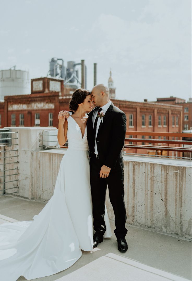 a bride and groom kissing on top of a roof in front of an industrial building