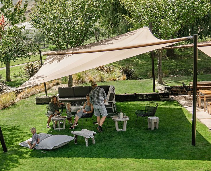 several people sitting on lawn chairs under an awning in the grass next to a picnic table