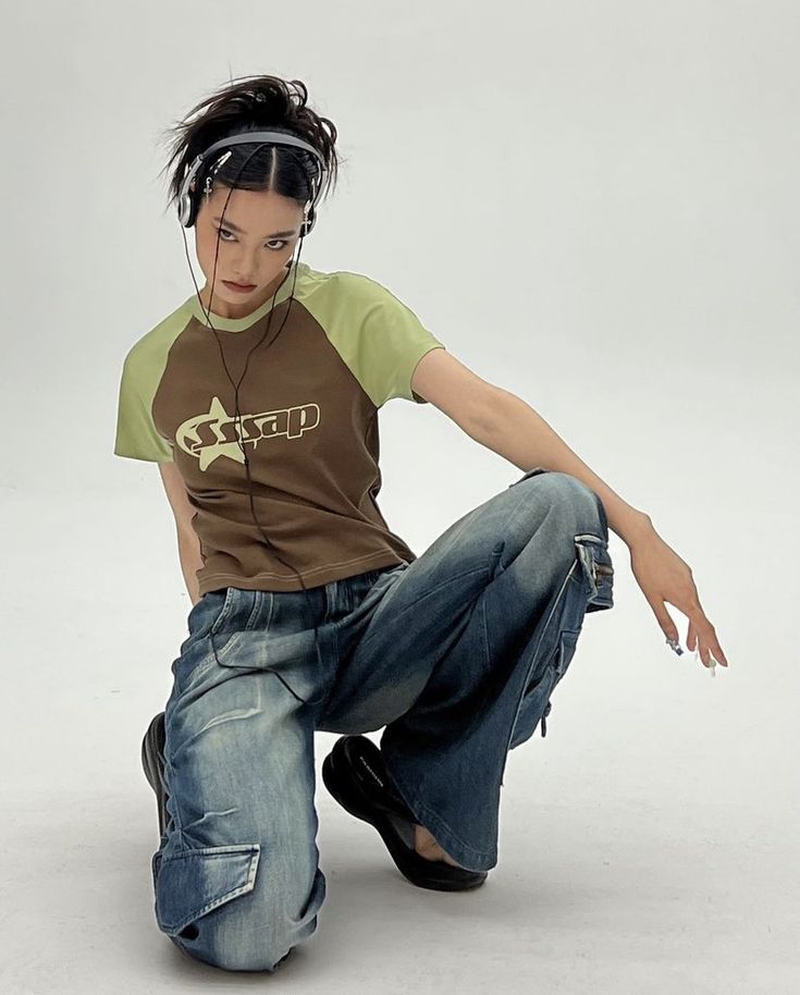 a young man sitting on the ground with headphones in his ears and wearing jeans