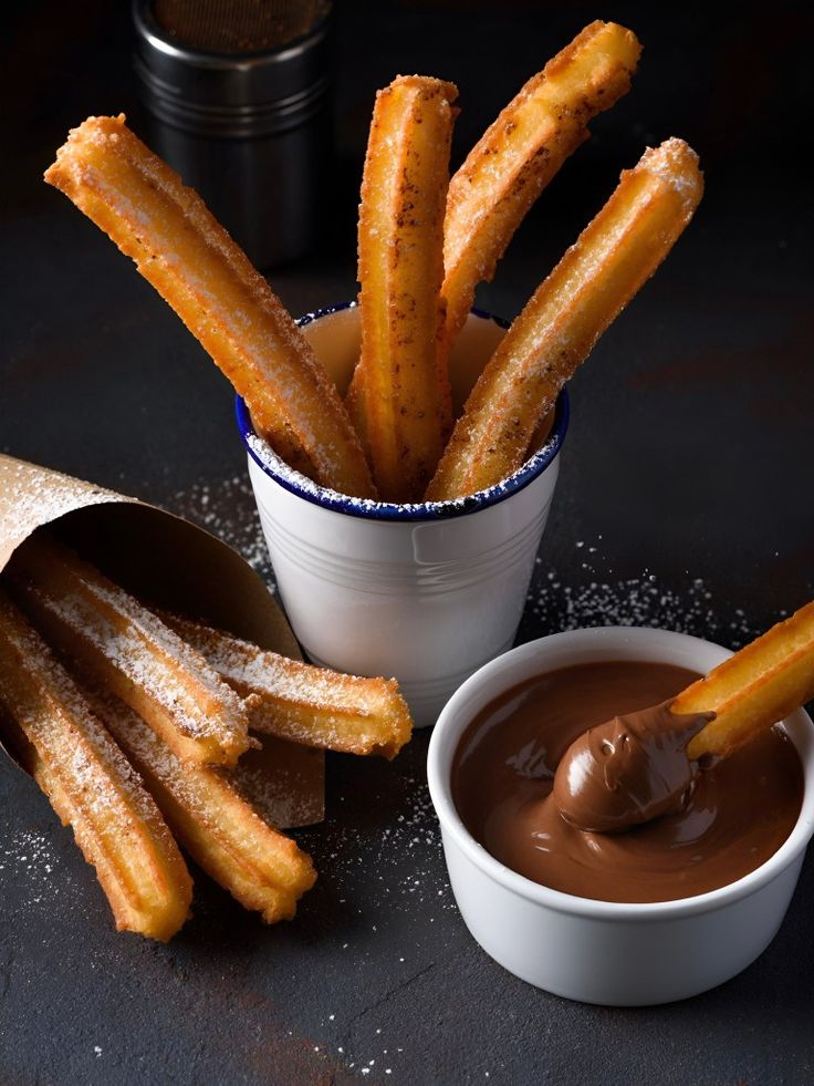 churro sticks being dipped with caramel sauce in a white bowl on a table