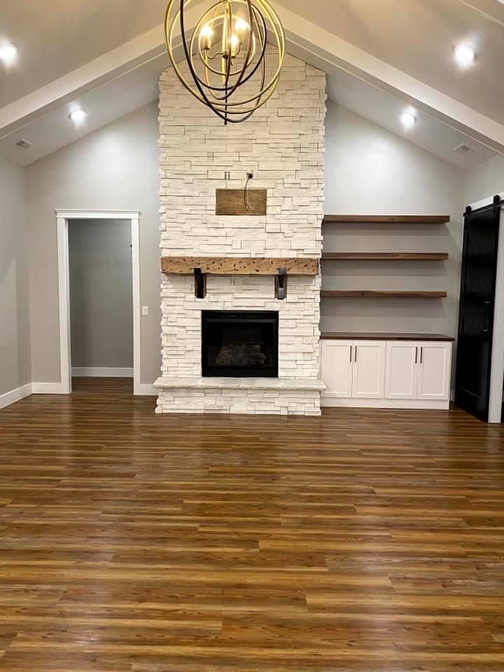 an empty living room with hard wood flooring and white brick fireplace in the center