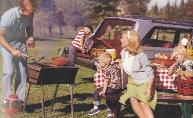 a family sitting at a picnic table in front of a car with the trunk open