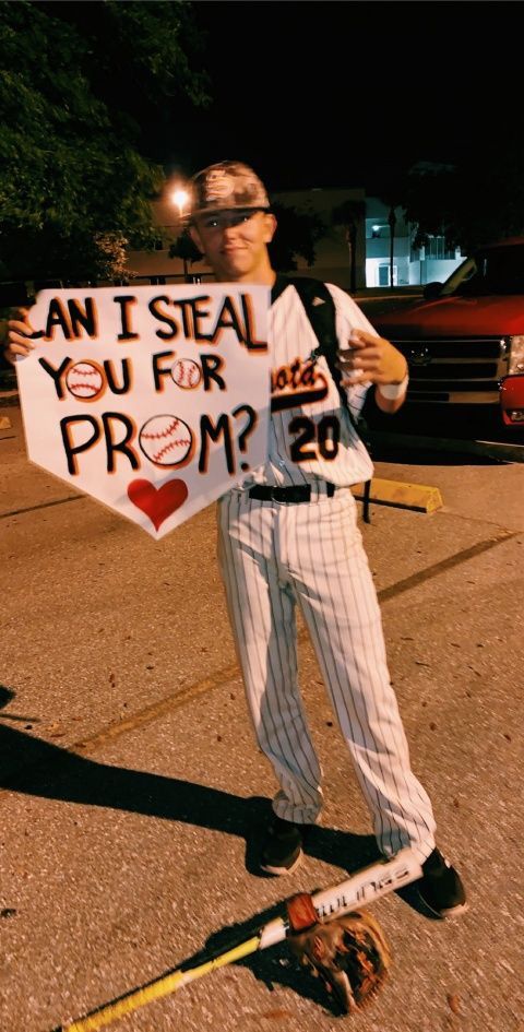 a baseball player holding a sign that says can't steal you for prom