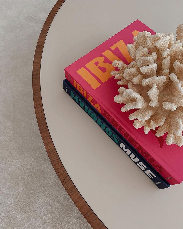 a stack of books sitting on top of a white table next to a pink book