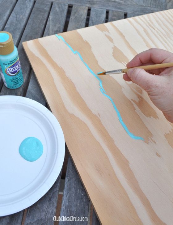 a person is painting wood with blue paint and a white plate on the table next to it