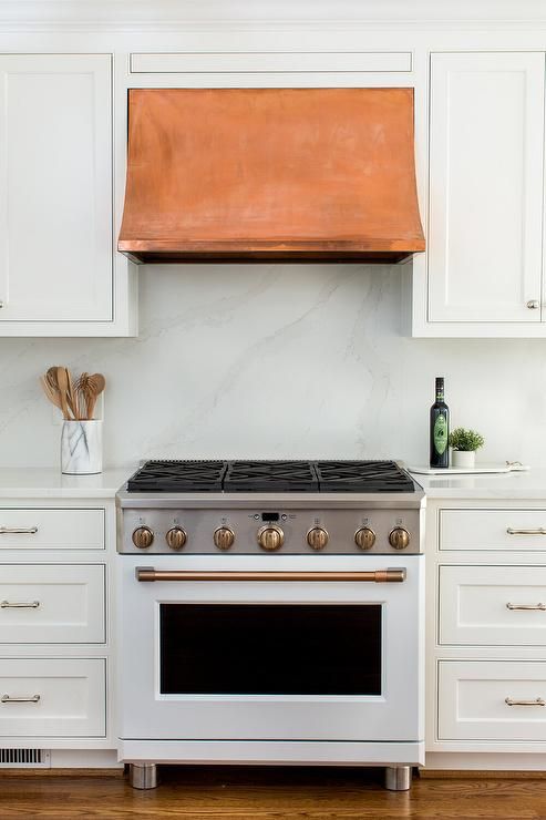 a kitchen with white cabinets and an copper range hood over the gas stove in front of it