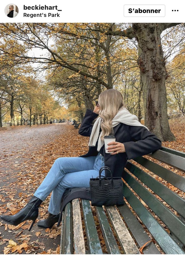 a woman sitting on top of a wooden bench next to a forest filled with trees