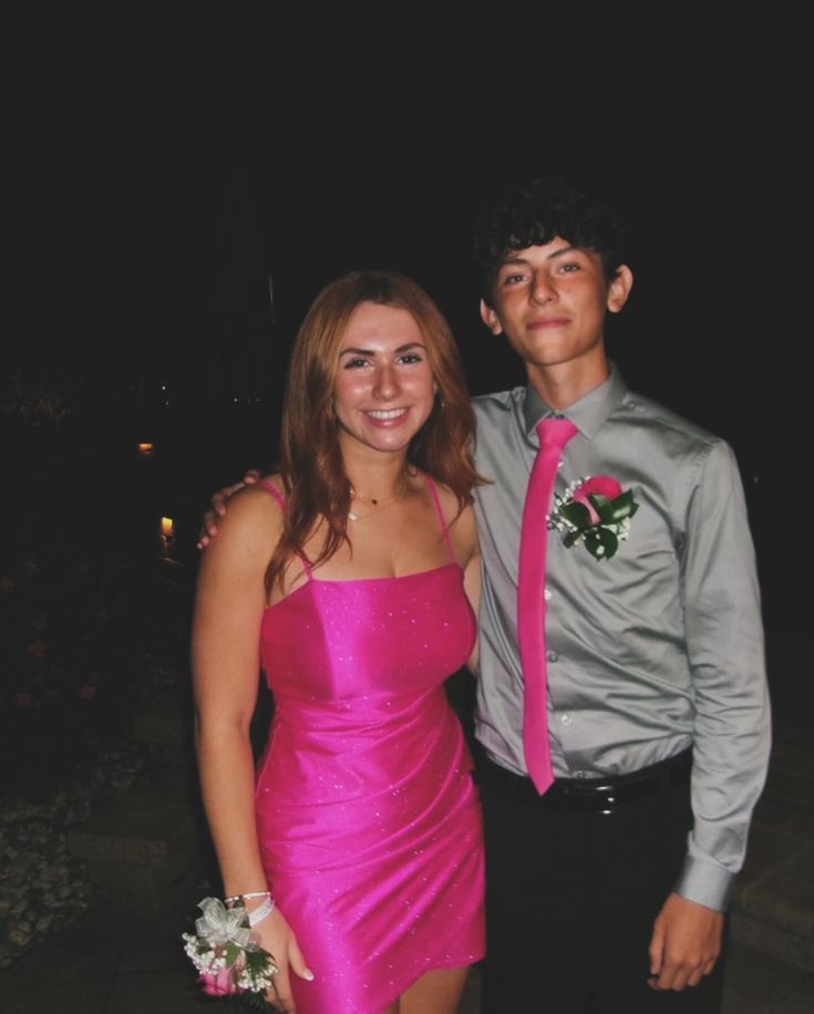 a young man standing next to a woman in a pink dress