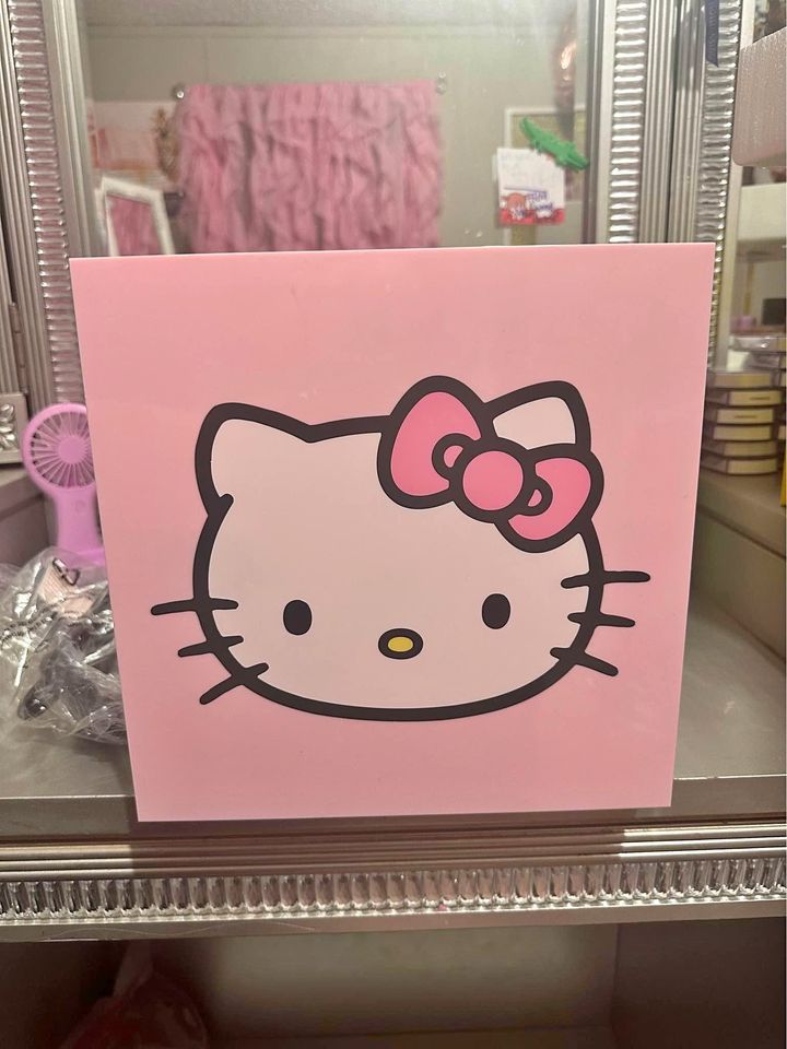 a pink hello kitty sign with a bow on it's head in front of a mirror