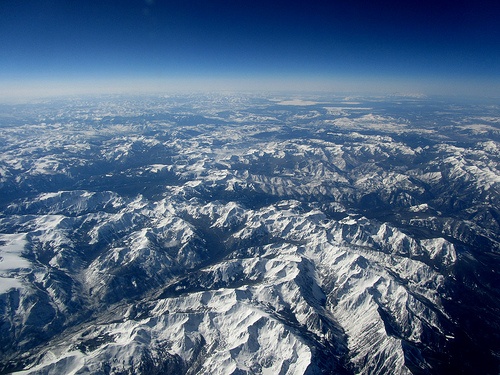 the view from an airplane looking down on snow covered mountains and blue skies in the distance