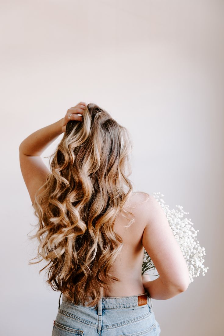 the back of a woman's head with long, wavy hair and flowers in her hair