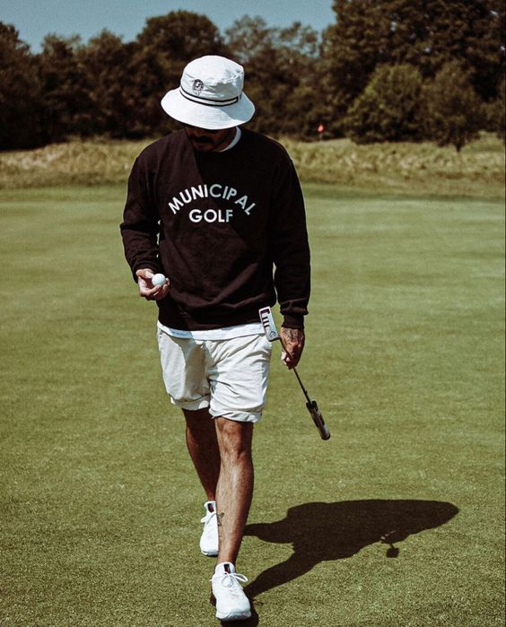 a man walking across a lush green field holding a golf racquet in his hand