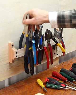 a person holding scissors and pliers in their hand on a wooden table with other tools