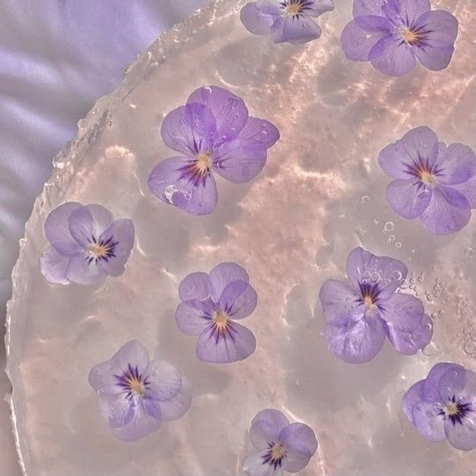 purple flowers floating in water on top of a white cake with frosting and icing