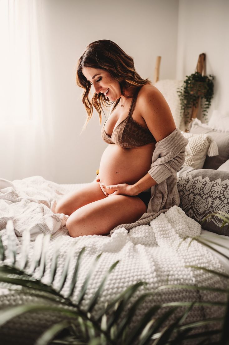 a pregnant woman sitting on a bed with her belly wrapped up and looking at the camera