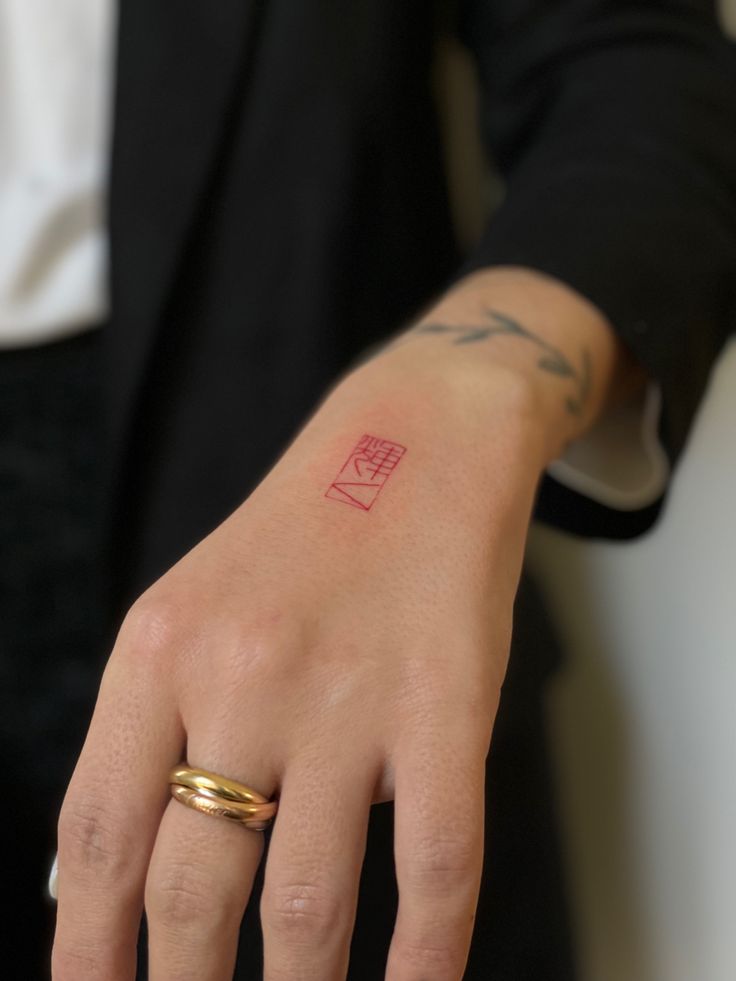 a person with a tattoo on their left hand and a gold band around the wrist