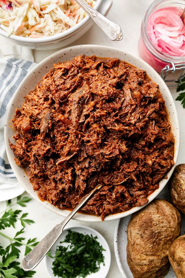 a bowl filled with shredded meat next to other food items on a white tablecloth