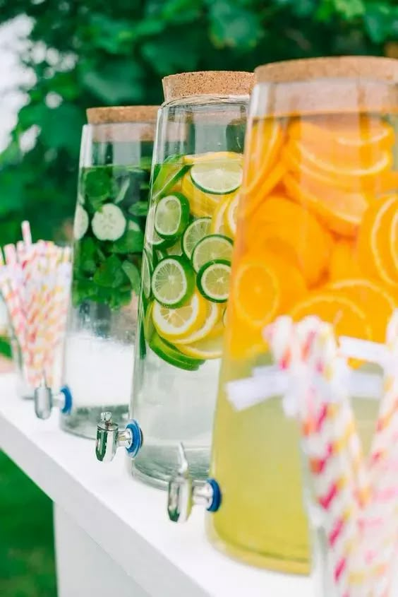 several glasses filled with lemonade and limeade sitting on a table in front of trees