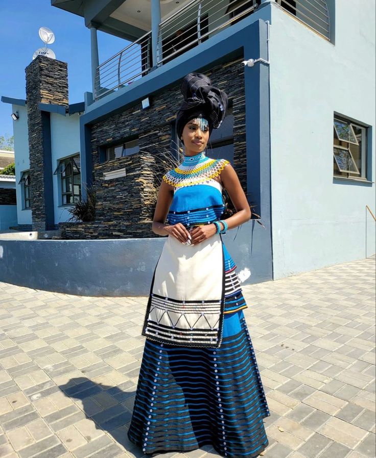 a woman is standing in front of a building wearing a blue and white dress with an african headdress