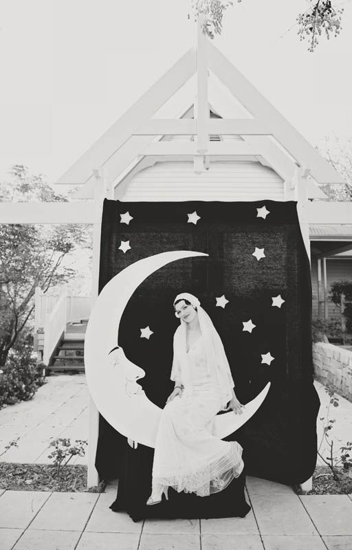 a black and white photo of a bride sitting on the moon in front of a house