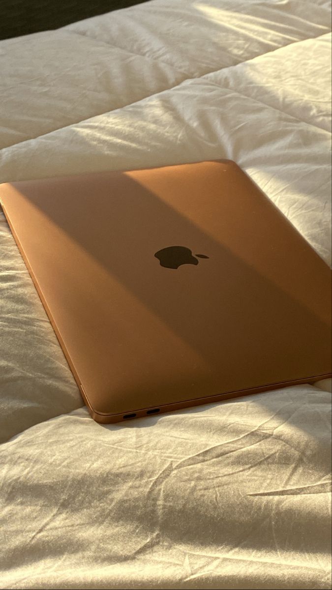 an apple laptop sitting on top of a white bed with the sun shining through it