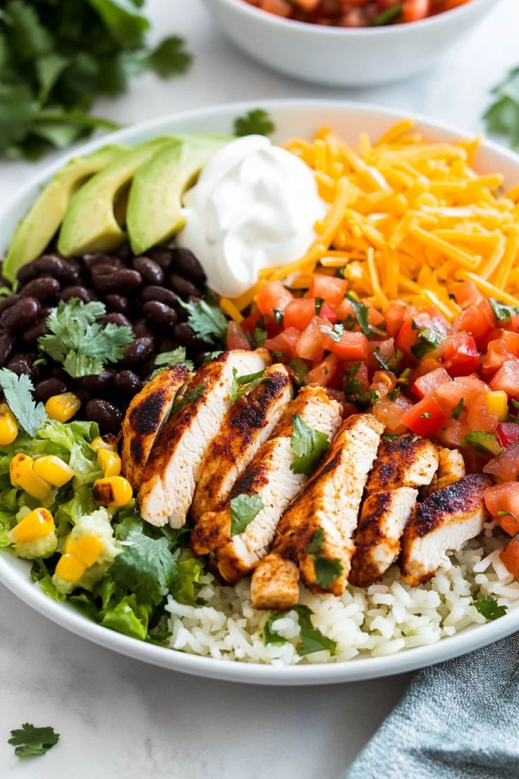 a white plate topped with chicken, rice and beans next to a bowl of salsa