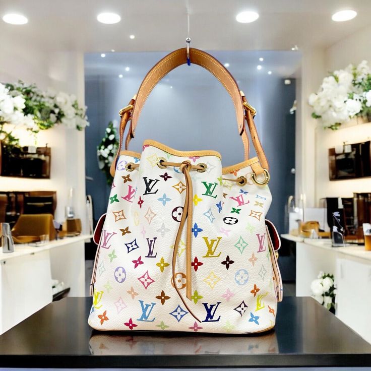 LOUIS VUITTON  Multicolore White Murakami Noe Petite Bucket Bag 100% Guaranteed Authentic  The Louis Vuitton Multicolor Monogram Petit Noé is a vibrant, stylish bucket bag featuring the classic monogram pattern in a spectrum of colors on white water resistant coated canvas. Its compact shape is both practical and chic, with leather trim, a drawstring closure, and an adjustable shoulder strap. Ideal for adding a pop of color to any outfit. Measurements Height 26cm (10.1in) Width 25cm (9.8in) Depth 18.5cm (7.2in) Drop of the Handle 25cm (9.8in) Shoulder Strap Length 64cm (25in) Hardware Golden-Tone Clean interior, scent free and clean  Leather brighter than most vintage pieces Great overall condition Minor marks on leather trim and strap  Minor marks on interior Minor marks on exterior canva Louis Vuitton Multicolor, Classic Monogram, Monogram Pattern, Vintage Pieces, Leather Trim, Leather Trims, Bucket Bag, Color Pop, Shoulder Strap