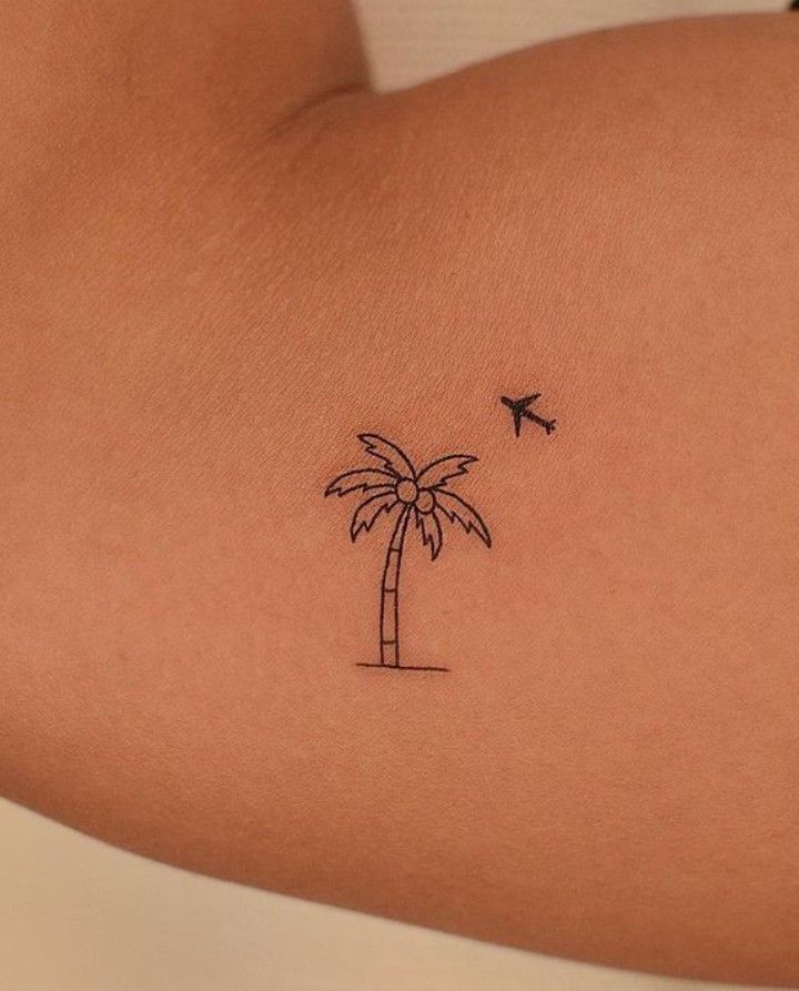 a small palm tree tattoo on the back of a woman's left arm with an airplane flying over it