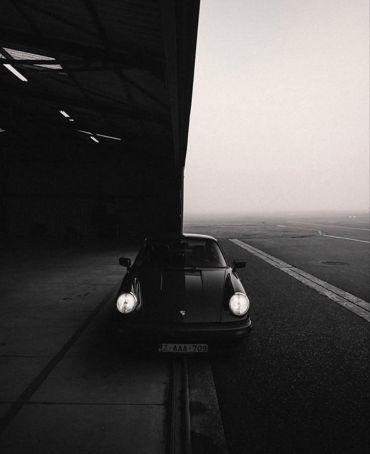 a black and white photo of a car parked on the side of an empty road