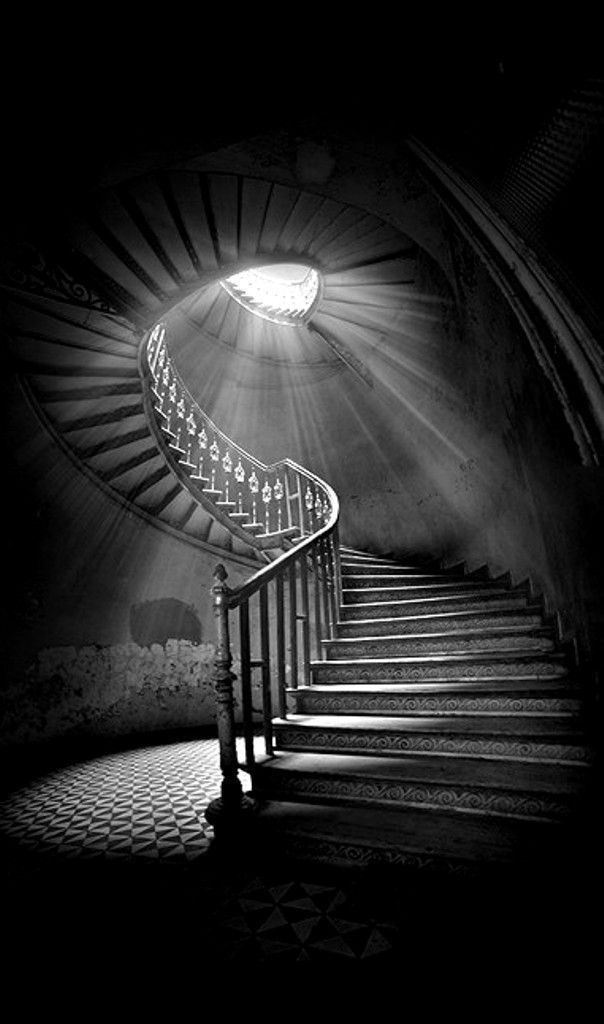 a spiral staircase with light coming from the top and below it in black and white