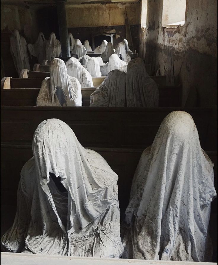 several statues covered in white cloths sitting on pews