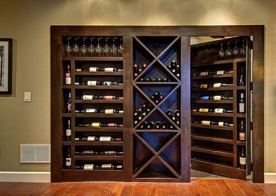 a wine cellar in the corner of a room with wooden floors and walls, along with two framed pictures on the wall