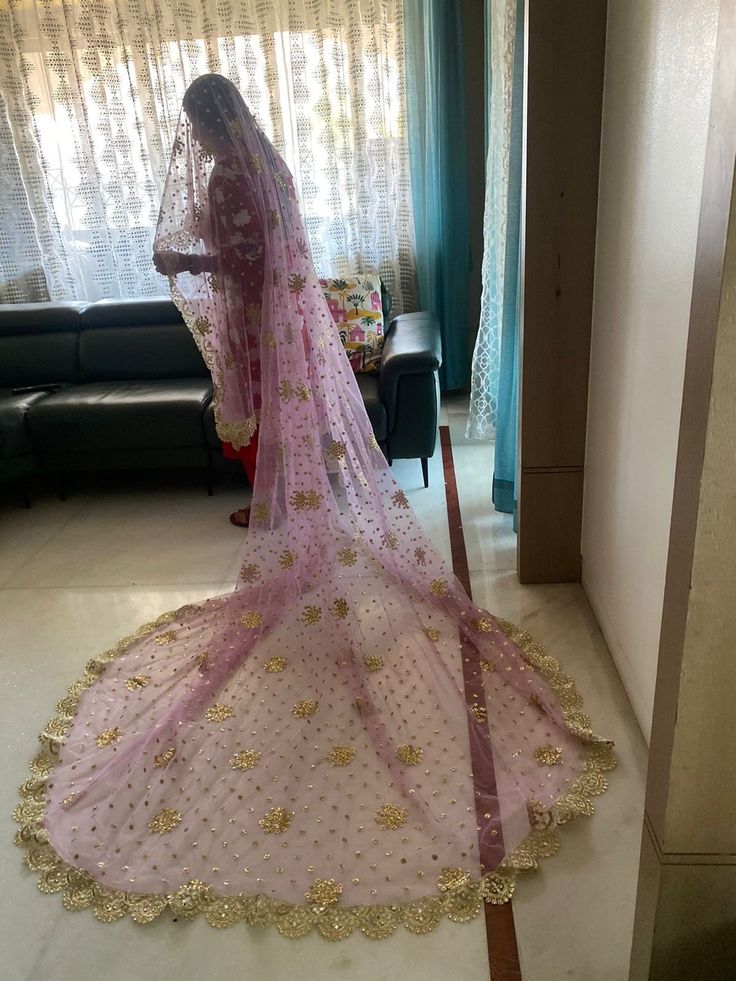 a woman in a pink and gold bridal gown looking at herself through the window