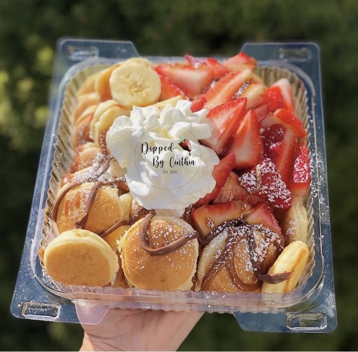 a person holding up a plastic container filled with desserts and pastries on top of it