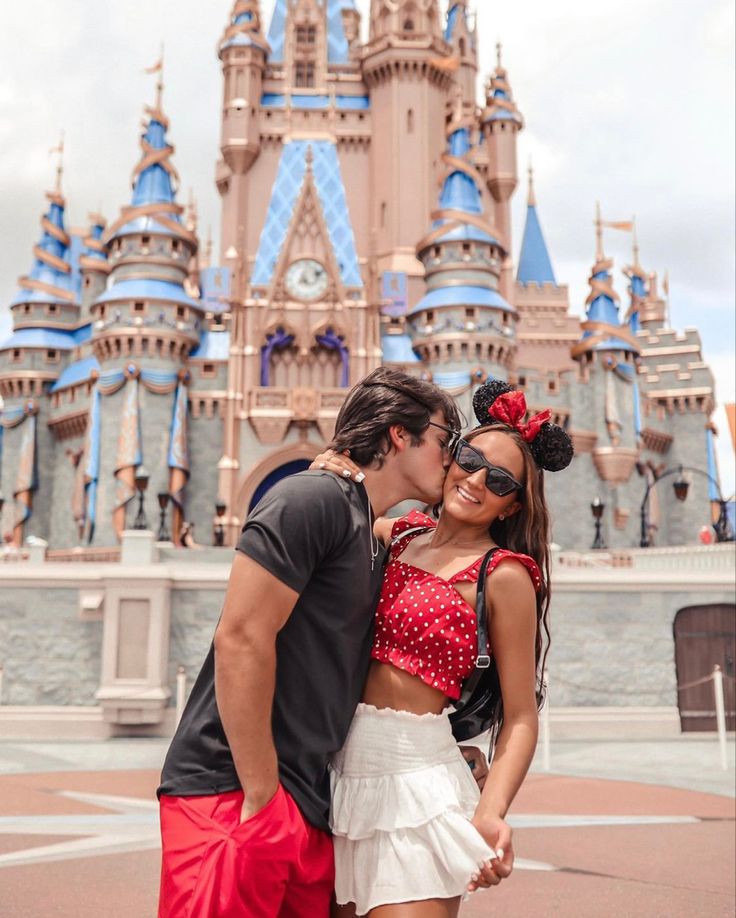 a man and woman kissing in front of a castle at disney world with their faces close to each other