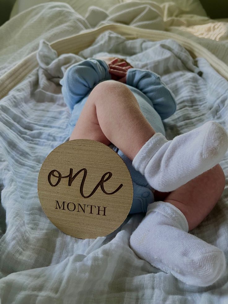 a baby laying on top of a bed next to a wooden sign that says one month