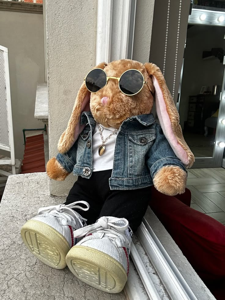 a stuffed rabbit wearing sunglasses sitting on top of a window sill next to a pair of sneakers