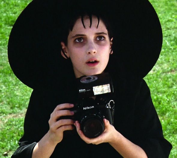 a young boy dressed in black holding a camera and taking a photo with his hat on